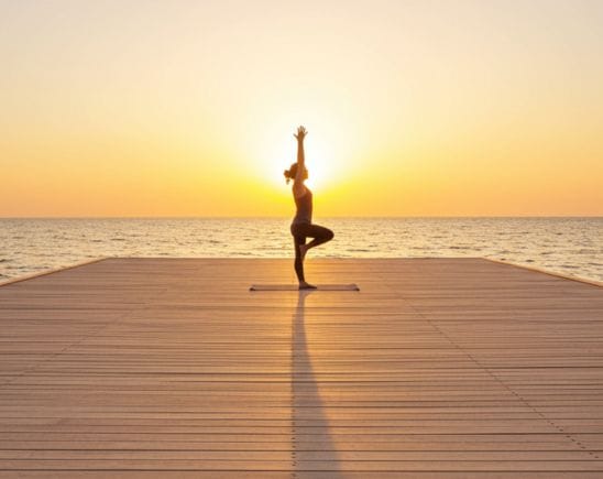 A woman on a boardwalk practicing a yoga pose at sunset.